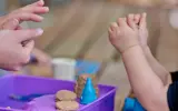 Een peuter speelt met wat zand samen met een van de medewerkers