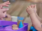 Een peuter speelt met wat zand samen met een van de medewerkers